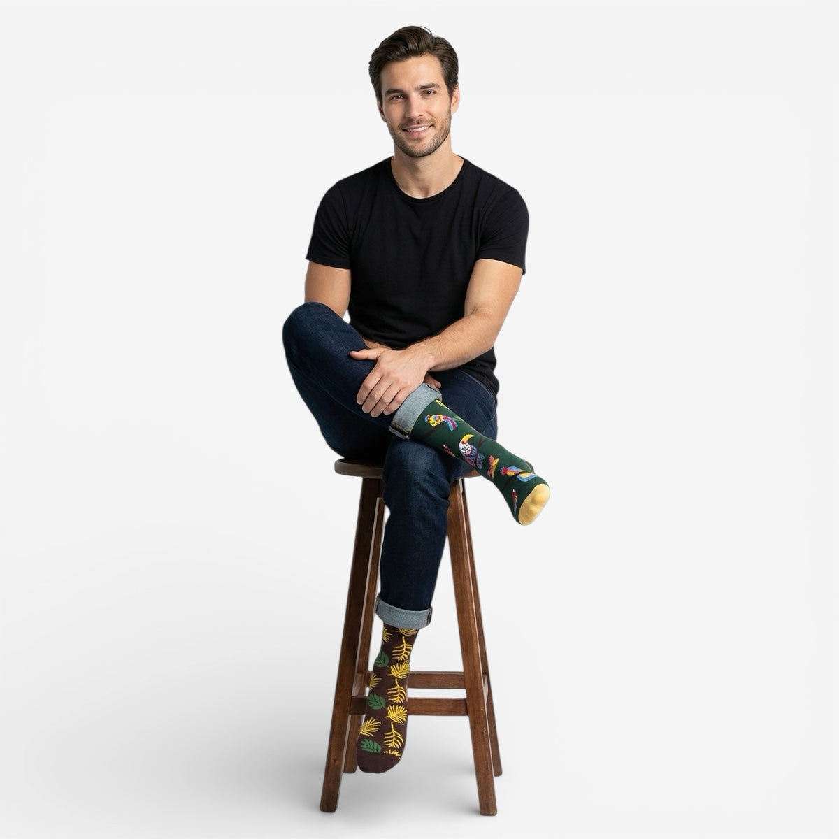 Man sitting on a stool wearing mismatched bird themed socks against a white background