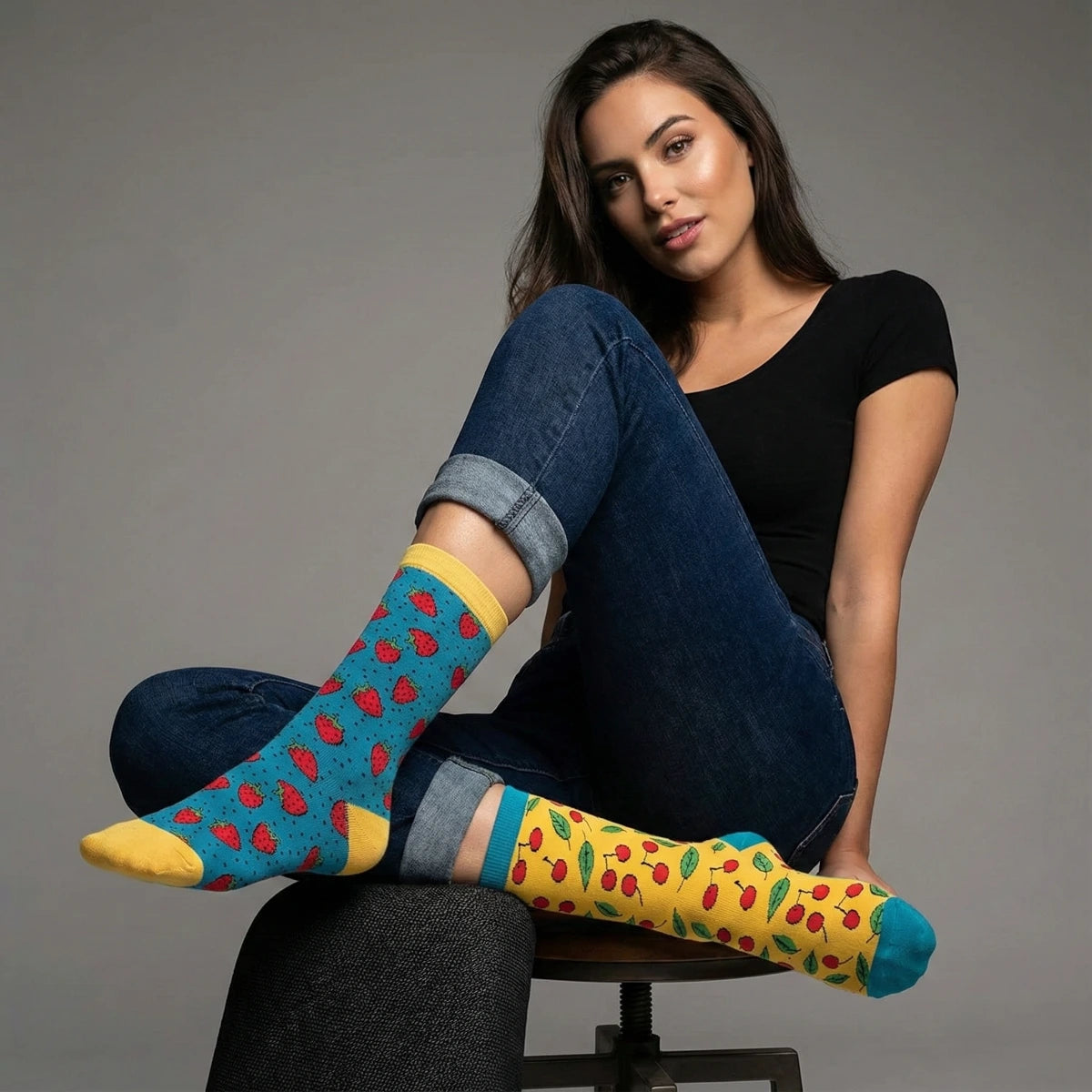 Woman wearing cherry themed socks sitting on a chair against a grey background
