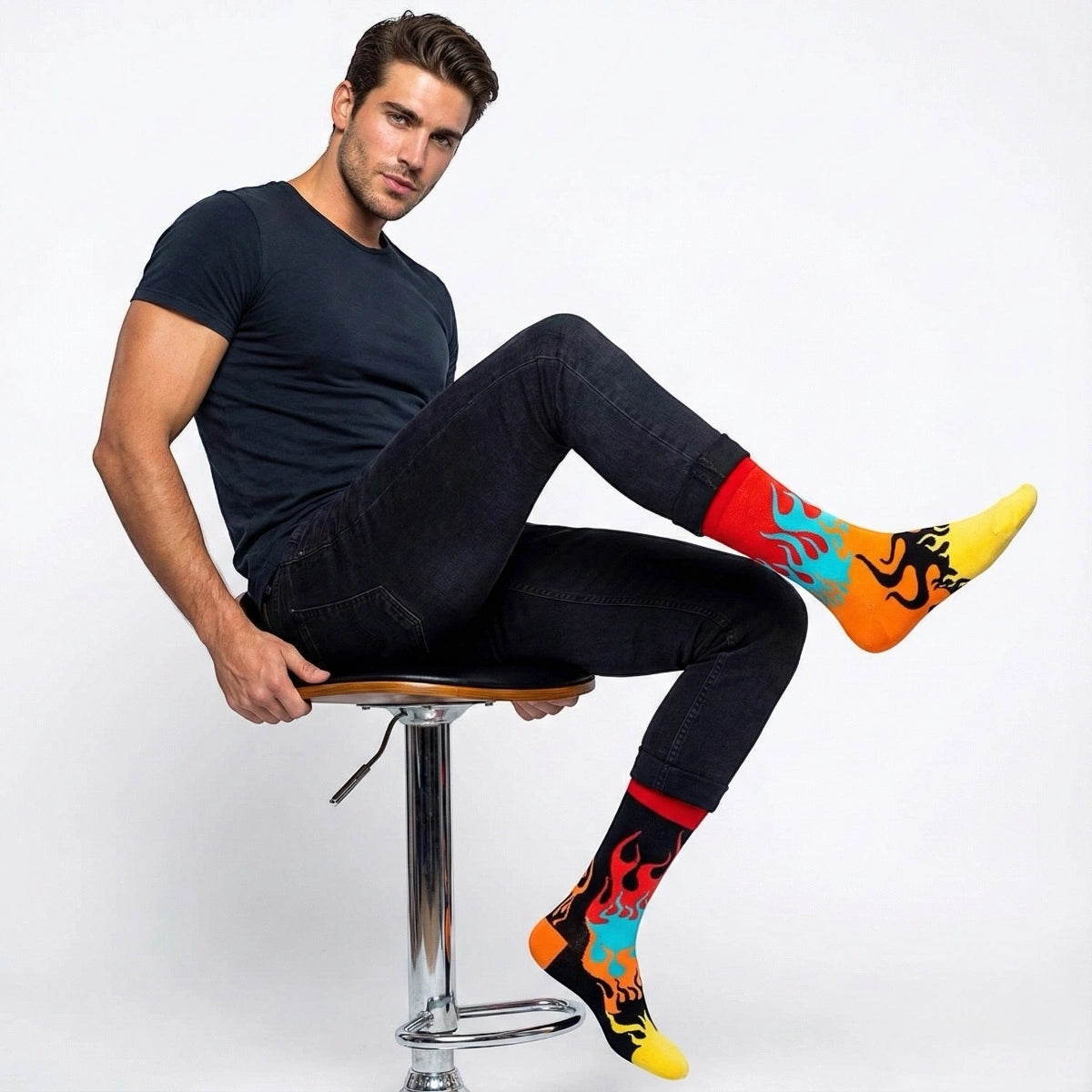 Man sitting on a stool wearing mismatched  fire themed socks with a white background