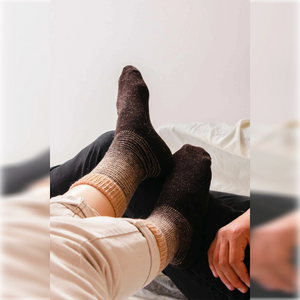 A woman wearing a pair of brown with beige stripe Alpaca and merino wool socks resting them on a man's legs