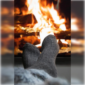 A person wearing a pair of plain charcoal Alpaca merino wool socks warming the feet in front of an open fire