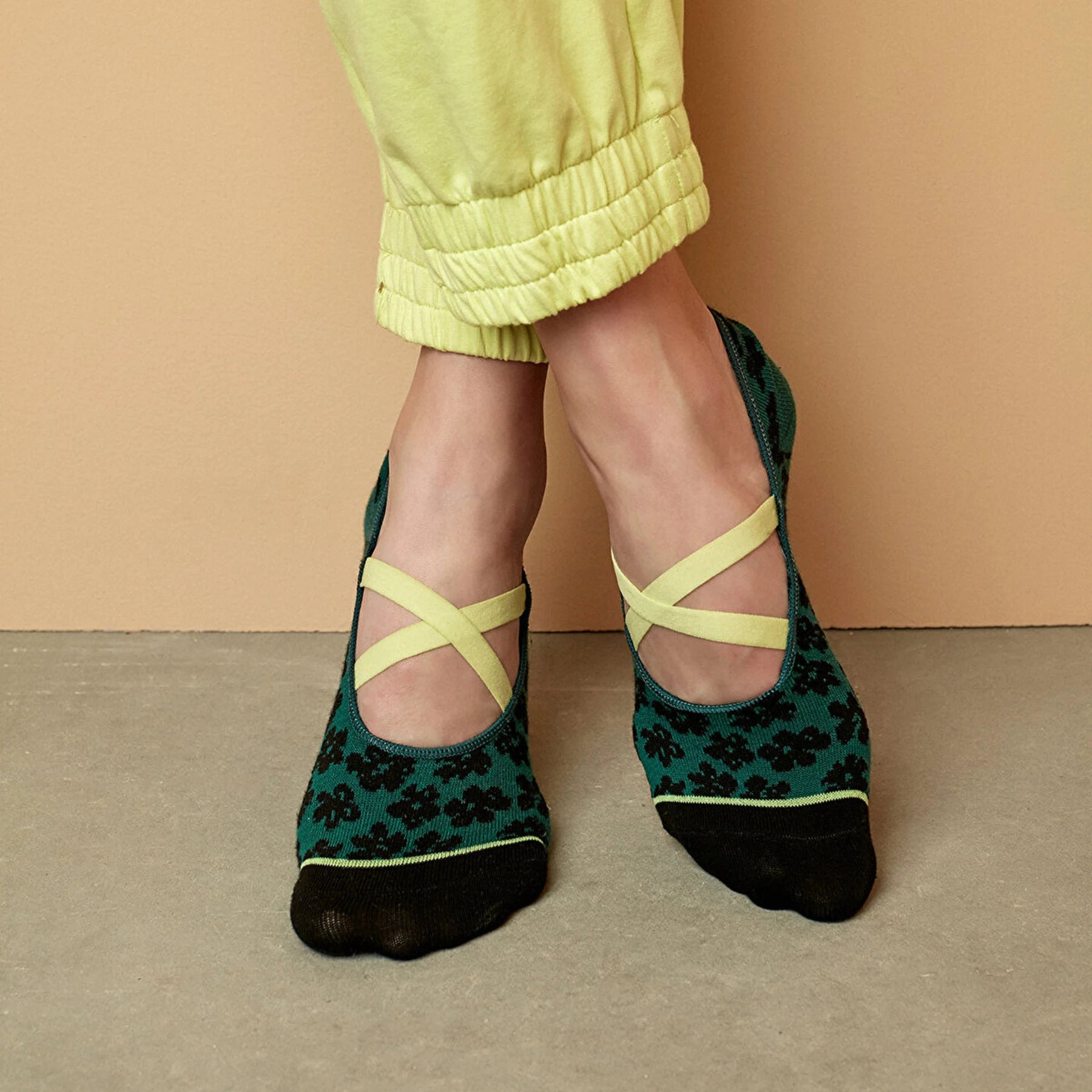 image of woman's legs wearing yellow sport pants and green floral yoga socks fitted with yellow elastic 