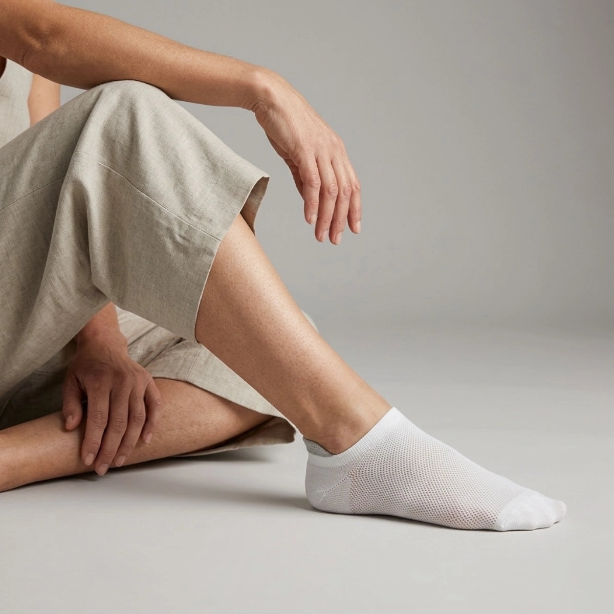 Person wearing white socks with grey heel tab sitting against a light backround