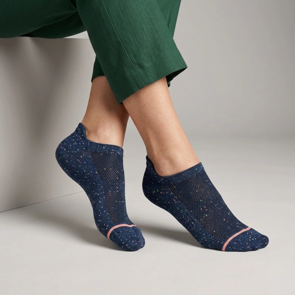 Blue socks with speckled accents worn by a person in green pants on a neutral background