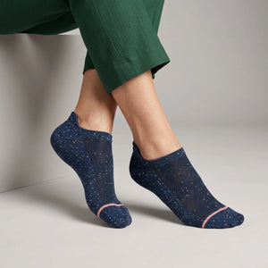 Blue socks with speckled accents worn by a person in green pants on a neutral background