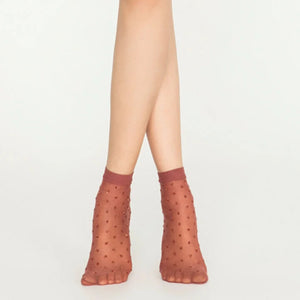 Woman wearing sheer cinnamon ankle socks with sparkling gold dots on white background