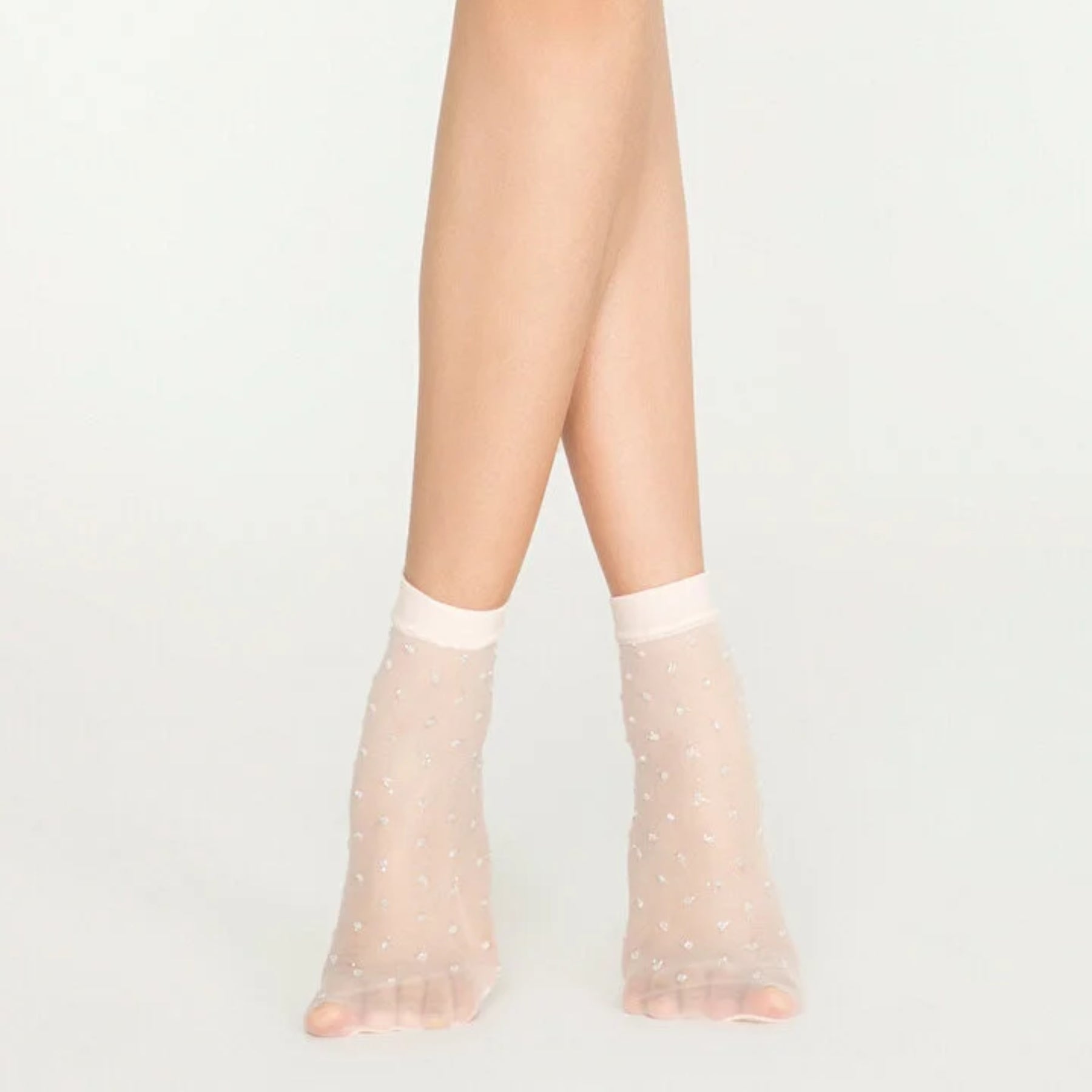Woman wearing sheer ivory ankle socks with sparkling gold dots on white background