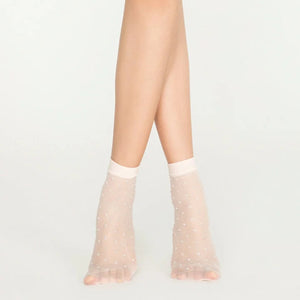 Woman wearing sheer ivory ankle socks with sparkling gold dots on white background