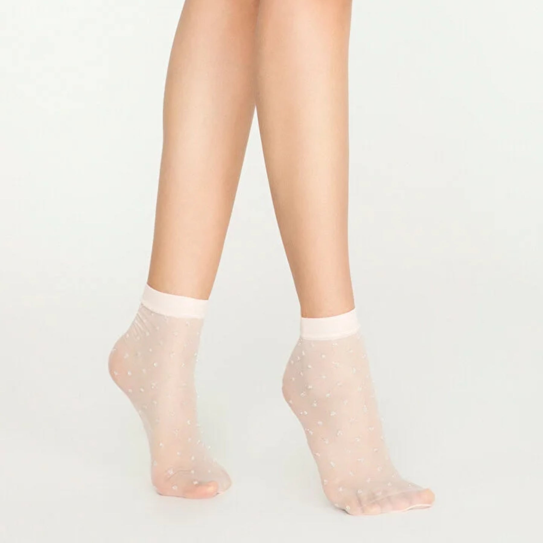 Woman wearing sheer ivory ankle socks with sparkling gold dots on white background