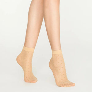 Woman wearing sheer nude ankle socks with sparkling gold dots on white background