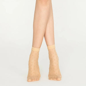 Woman wearing sheer nude ankle socks with sparkling gold dots on white background