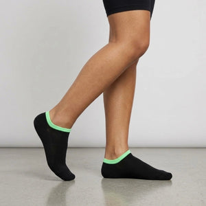 Person wearing black seamless ankle socks with green cuff against a neutral background