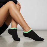 Person wearing black seamless ankle socks with green cuff against a neutral background