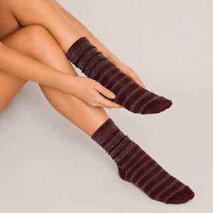 Burgundy glitter stripe women’s crew socks with shimmering metallic detail, styled in a relaxed seated fashion pose