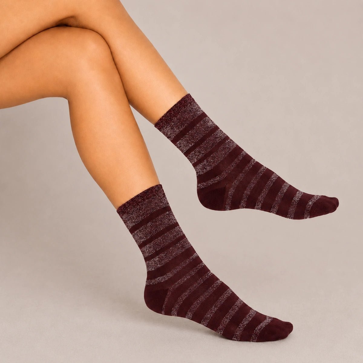 Burgundy striped women’s crew socks with metallic shimmer detail, styled in a crossed-leg pose against a neutral studio background