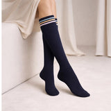 Navy knee-high socks with striped cuffs worn by a person sitting on a light-colored couch.