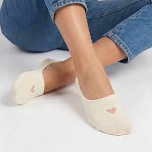 Person in jeans wearing a cream no-show sock with a beige heart design on a light grey background