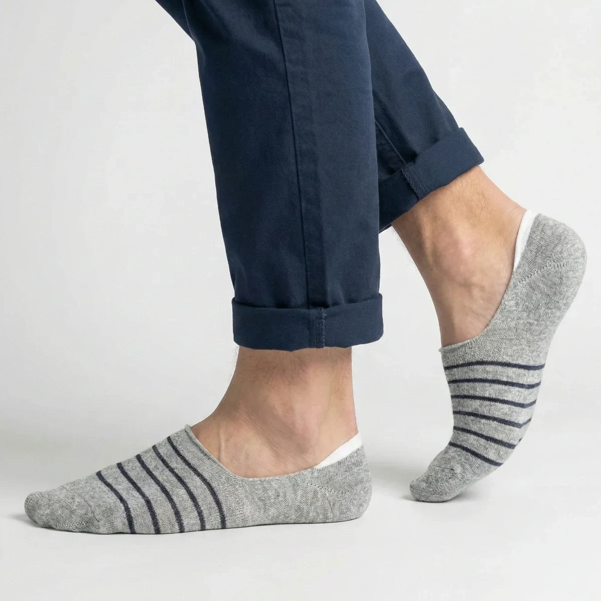 Grey no-show socks with black stripes worn with rolled-up navy pants on a light grey background
