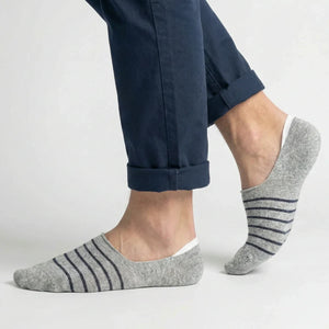 Grey no-show socks with black stripes worn with rolled-up navy pants on a light grey background