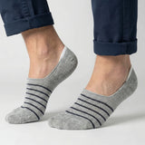 Grey no-show socks with black stripes worn with rolled-up navy pants on a light grey background