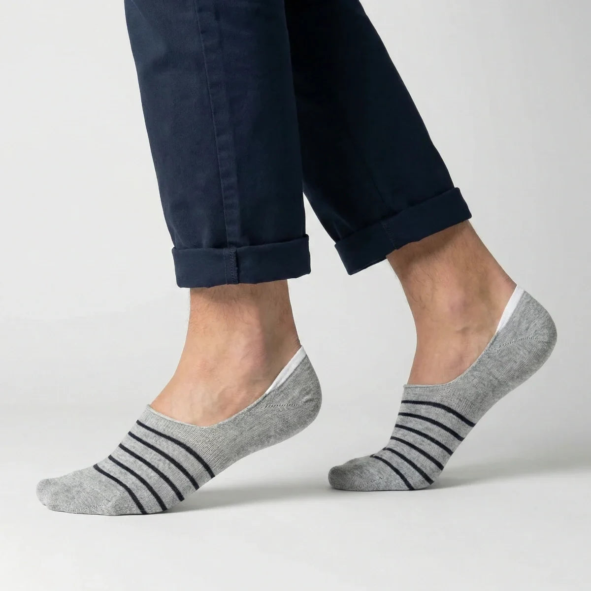 Grey no-show socks with black stripes worn with rolled-up navy pants on a light grey background