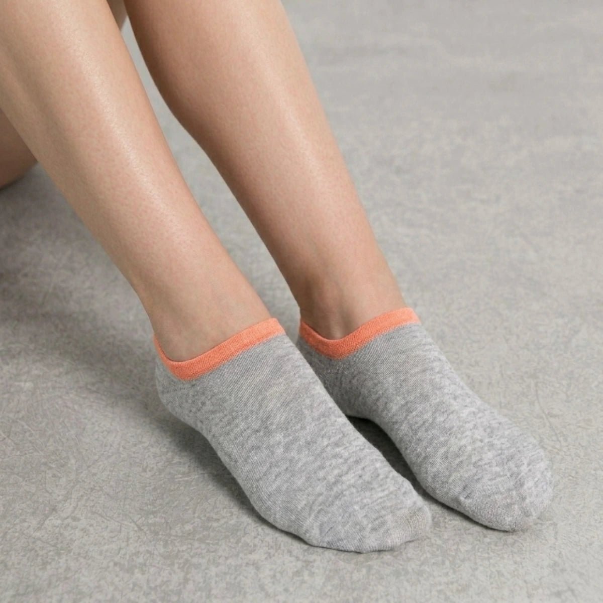 Person wearing grey no-seam ankle socks with orange cuff against a light background