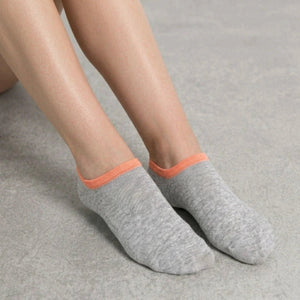 Person wearing grey no-seam ankle socks with orange cuff against a light background