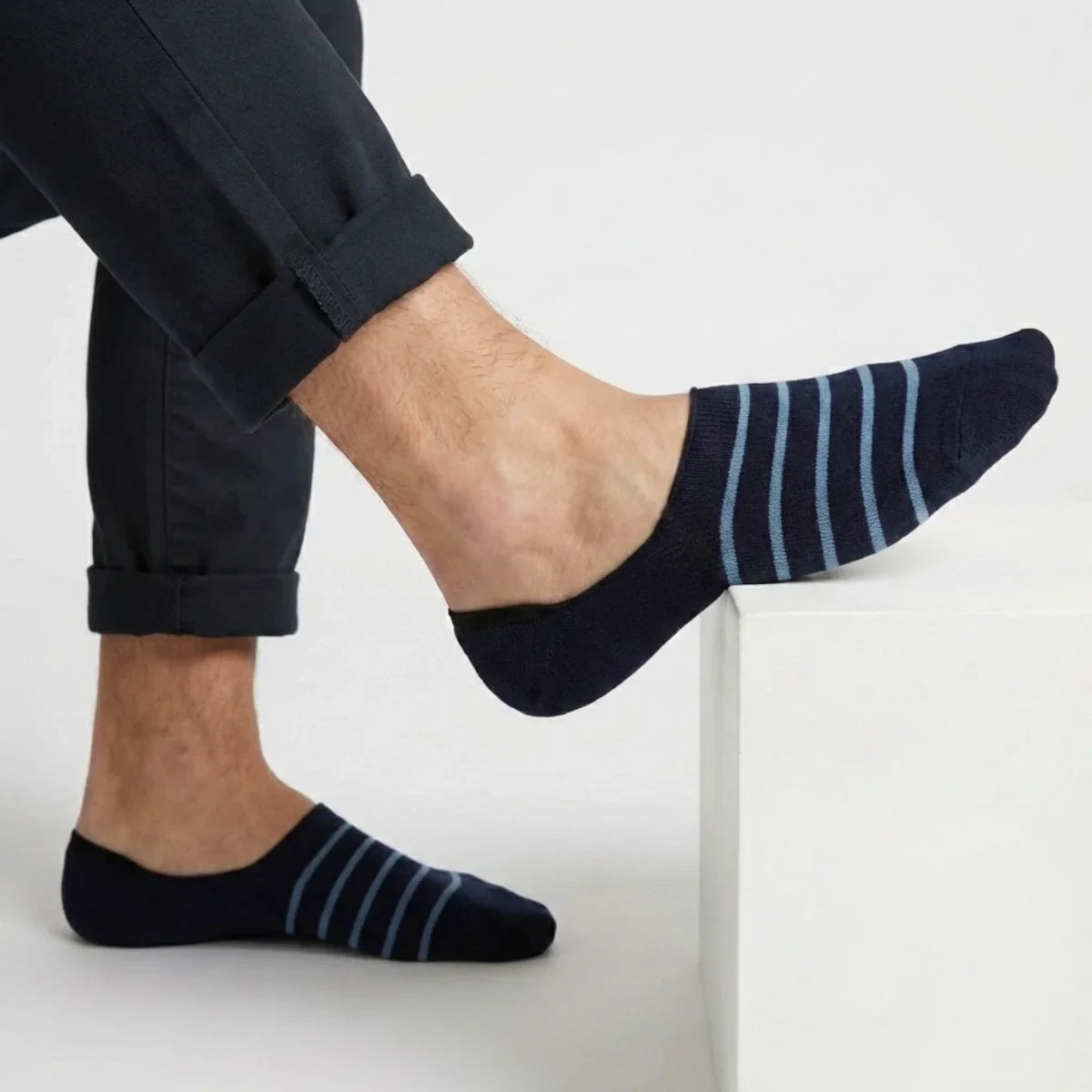 Navy with lighter blue stripe no-show socks worn with rolled-up dark pants on a light background