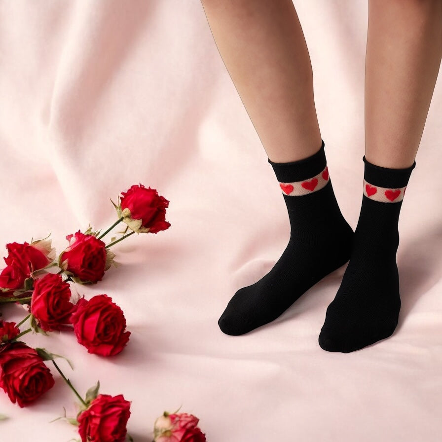 Woman's feet showing quarter length black socks with sheer cuff adorned with red love hearts, standing on a sheet with red roses at her feet