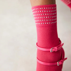 Close-up of a woman leg showing bright pink quarter length socks, cuffed with six rows of shiny dots wearing matching coloured open shoes