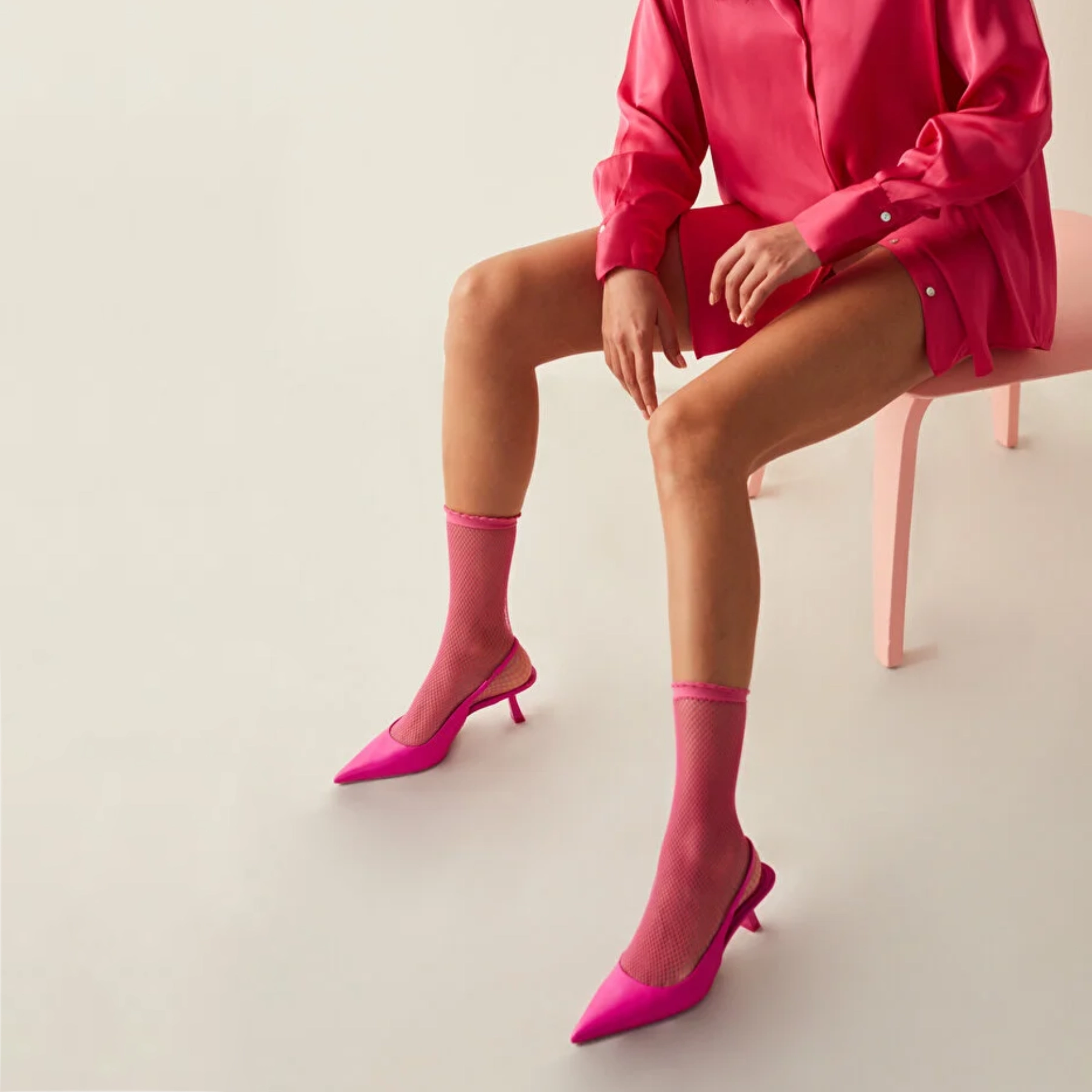 Woman sitting on a pink chair wearing a bright red silky shirt and fuchsia quarter length mesh socks with matching open shoes