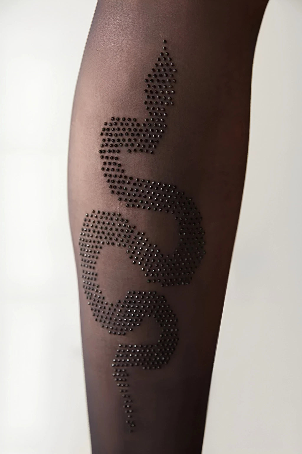 Close-up of black sheer tights featuring a rhinestone snake design on the calf.