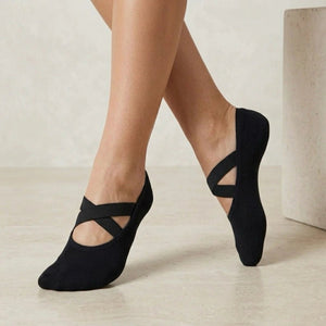 Person wearing black yoga socks with crisscross straps on a neutral background
