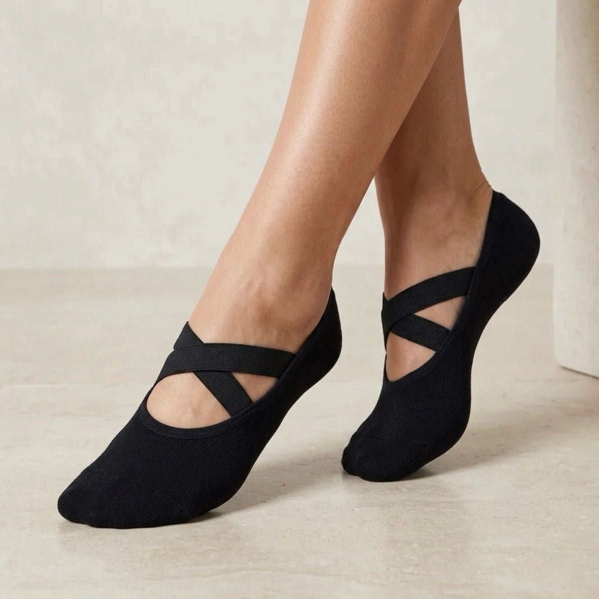 Person wearing black yoga socks with crisscross straps on a neutral background