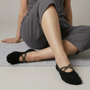 Person wearing black yoga socks with a crisscross brand logo strap on a neutral background