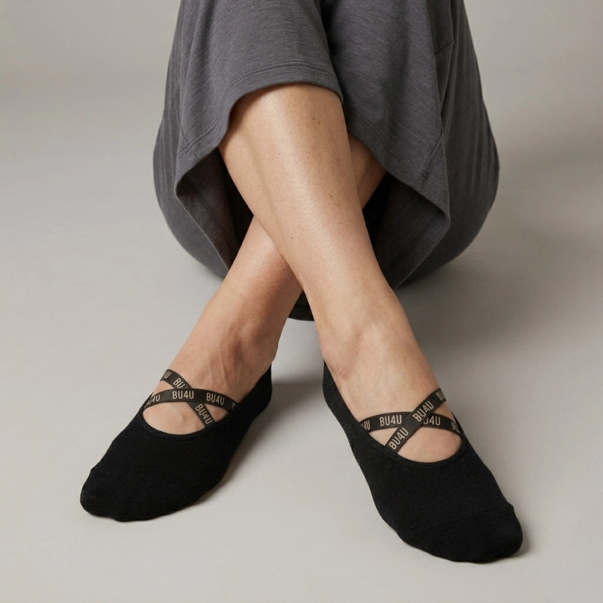 Person wearing black yoga socks with a crisscross brand logo strap on a neutral background
