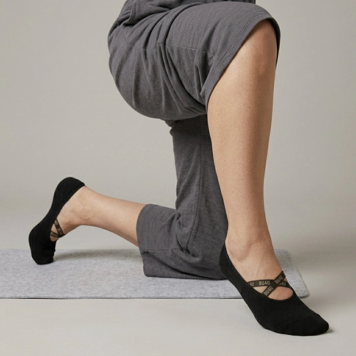 Person wearing black yoga socks with a crisscross brand logo strap on a neutral background