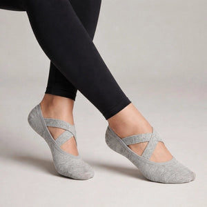 Person wearing grey yoga socks with crisscross straps and black leggings on a neutral background