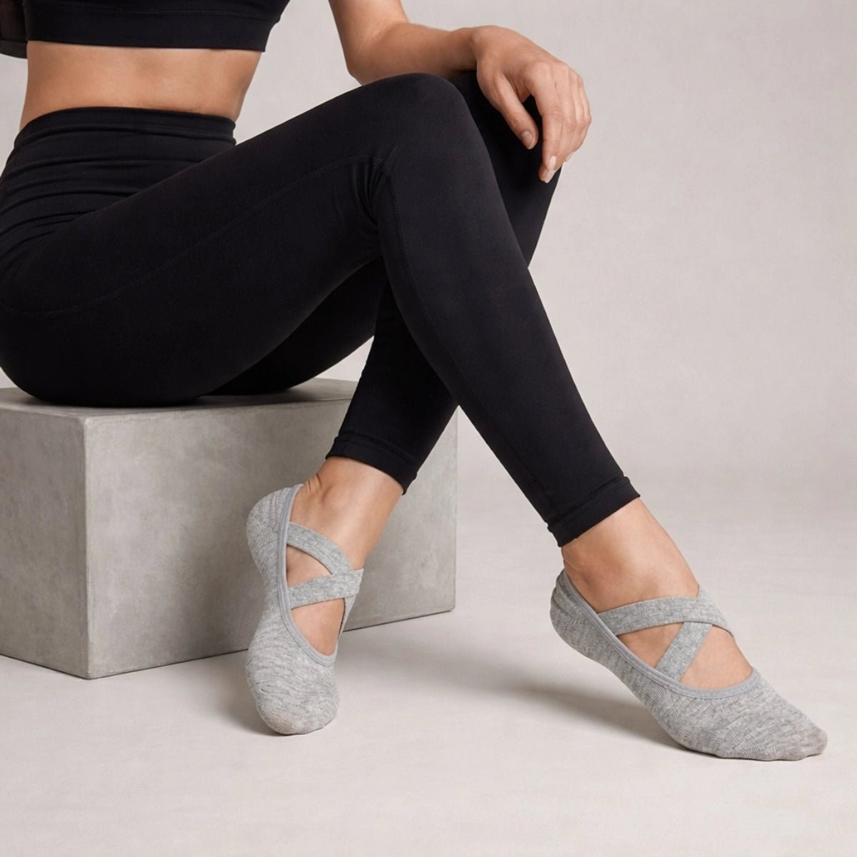 Person wearing grey yoga socks with crisscross straps and black leggings on a neutral background