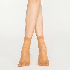 A close-up of a woman's legs wearing tan, dotted nude socks, showcasing a stylish and casual look.