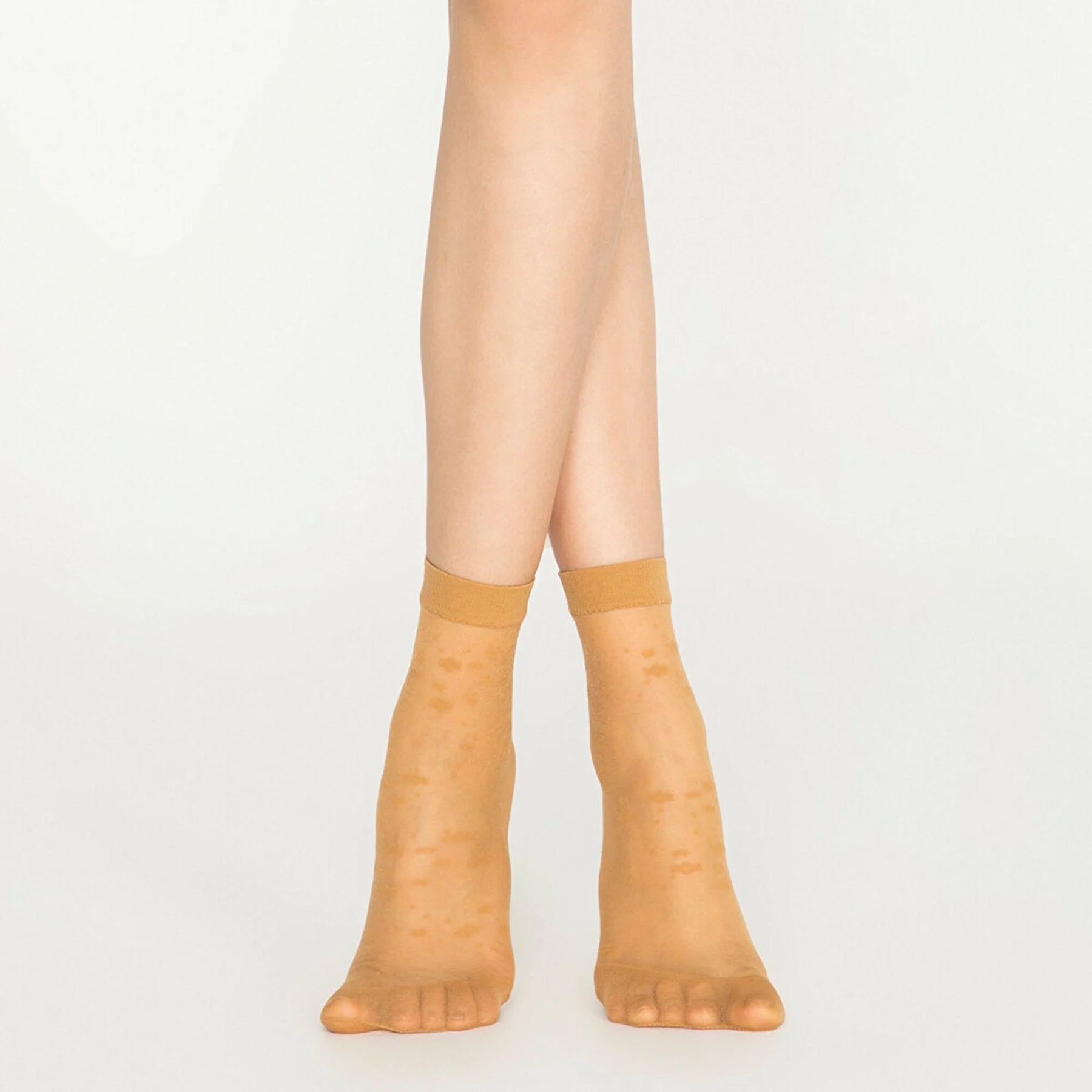 A pair of legs in tan nude socks with dots, emphasizing a chic and relaxed aesthetic.